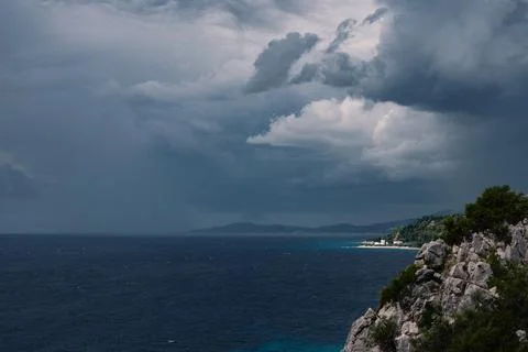 Dramatic dark storm clouds loom over a deep blue sea and rocky coastline in.. 库存照片
