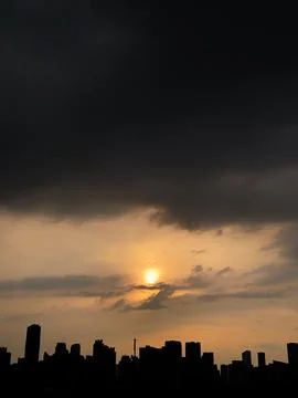 Dramatic dark storm clouds over city skyline silhouette at sunset Stock Photos