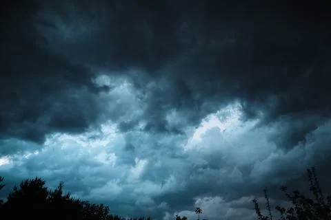 Dramatic dark storm clouds in sky over forest silhouette before rain close up Stock Photos