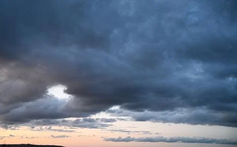 Dramatic dark storm clouds at sunset with a small light opening. Stock Photos