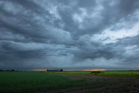 Dramatic dark storm clouds sweep over a flat rural farmland Stock Photos