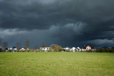 Dramatic dark storm sky approaching houses on horizon over meadow Stock-Fotos