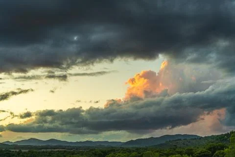 Dramatic dark stormy sky with yellow sunset-colored cloud above scenic landsc Stock Photos