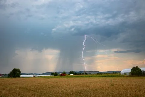 Dramatic daytime lightning strike with dark clouds and rain shaft Stock Photos