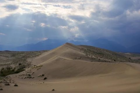 Dramatic desert dunes under sunbeams and cloudy sky Stock Photos