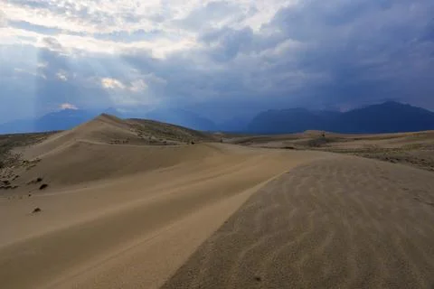 Dramatic desert dunes under sunbeams and cloudy sky Stock Photos