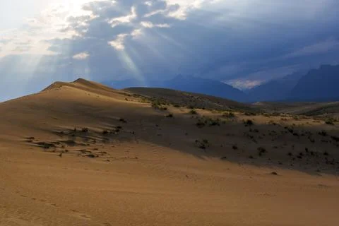 Dramatic desert dunes under sunbeams and cloudy sky Stock Photos