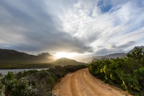 Dramatic dirt road into the mountain range at sunset Stock Photos