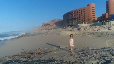 Dramatic drone pull out from female model on rocky beach surf sunrise Stock Footage 104888167