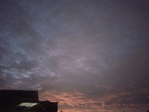 Dramatic dusk sky with dark purple clouds, orange sunset glow, and building Stock Photos