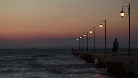 Dramatic Dusk View of Long Concrete Pier, Rough Sea Waves, and Illuminated Lamps 스톡 동영상 319485942