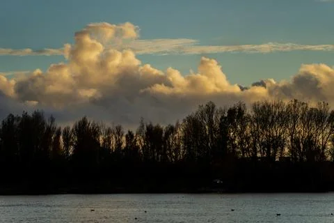 Dramatic evening clouds above calm river with autumn trees Stock Photos