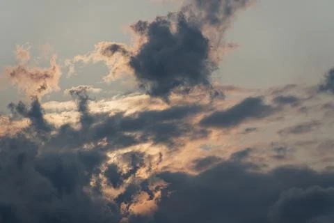 Dramatic evening clouds with soft pink glow and hidden sun Stock Photos