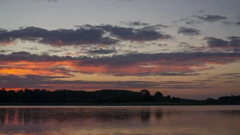 Dramatic evening sunset over a calm lake with dark clouds and forest silhouette 스톡 동영상 346180448