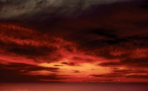 Dramatic fiery red sunset over the ocean horizon with dramatic clouds 스톡 사진