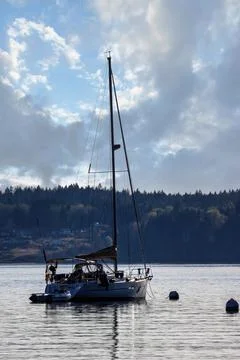 Dramatic glowing clouds in late afternoon over calm water and sailboat Stock Photos