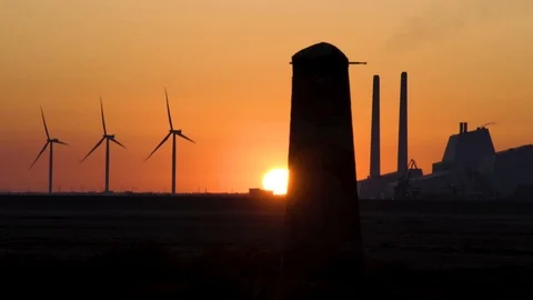 Dramatic golden red sunset behind green energy wind turbines and fossil fuel  Stock Footage 107051006