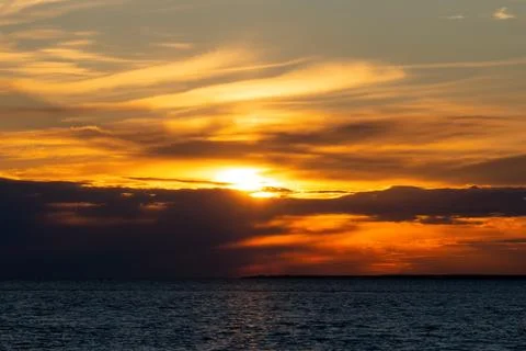 Dramatic golden sunset over calm sea with dark clouds cutting through sun. .. Stock Photos