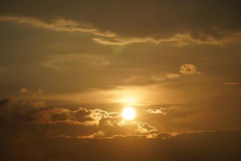 Dramatic golden sunset over calm water with sun rays breaking through clouds Stock Photos