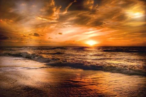Dramatic Golden Sunset Over Ocean Waves and Sandy Beach Stock Photos