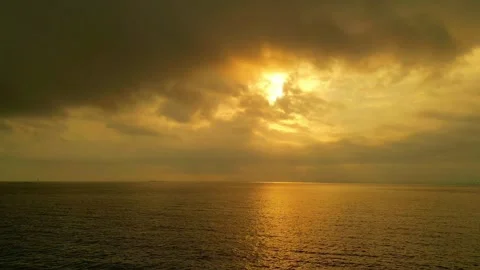 Dramatic Golden Sunset over Open Ocean with Sun Rays Through Dark Clouds Stock Footage 320034883