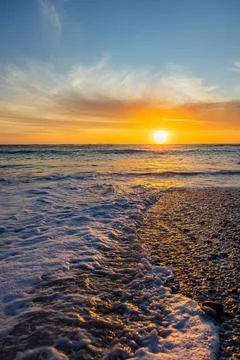 Dramatic Golden sunset over tranquil beach, waves lashing the pebble coastlin Stock Photos