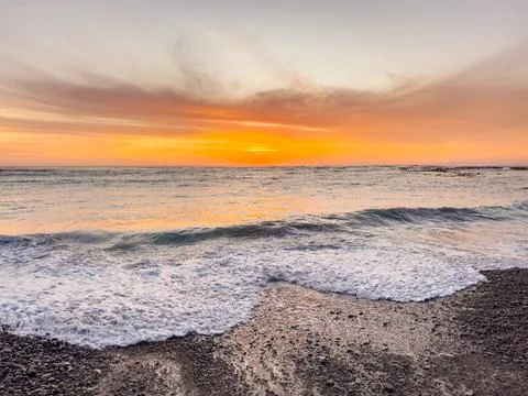 Dramatic Golden sunset over tranquil beach, waves lashing the pebble coastlin Stock Photos