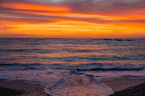 Dramatic Golden sunset over tranquil beach, waves lashing the pebble coastlin Stock Photos