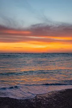 Dramatic Golden sunset over tranquil beach, waves lashing the pebble coastlin Stock Photos