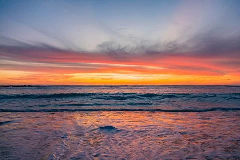 Dramatic Golden sunset over tranquil beach, waves lashing the pebble coastlin Stock Photos