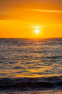 Dramatic Golden sunset over tranquil beach, waves lashing the pebble coastlin Stock Photos
