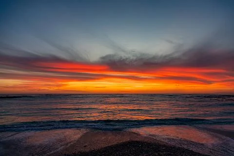 Dramatic Golden sunset over tranquil beach, waves lashing the pebble coastlin Stock Photos