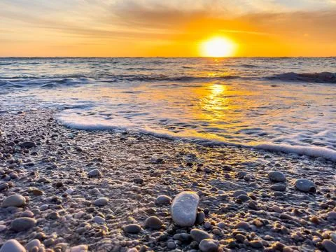 Dramatic Golden sunset over tranquil beach, waves lashing the pebble coastlin Stock Photos