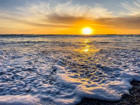 Dramatic Golden sunset over tranquil beach, waves lashing the pebble coastlin Stock Photos