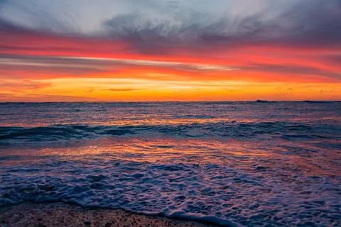 Dramatic Golden sunset over tranquil beach, waves lashing the pebble coastlin Stock Photos