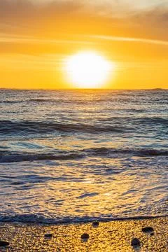 Dramatic Golden sunset over tranquil beach, waves lashing the pebble coastlin Stock Photos