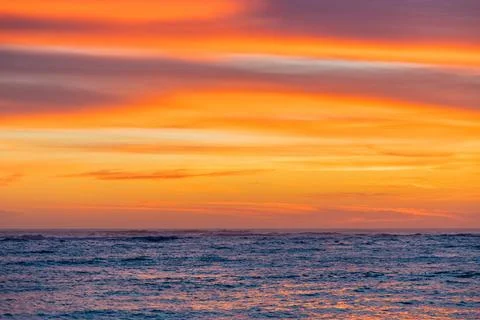 Dramatic Golden sunset over tranquil beach, waves lashing the pebble coastlin Stock Photos