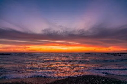 Dramatic Golden sunset over tranquil beach, waves lashing the pebble coastlin Stock Photos