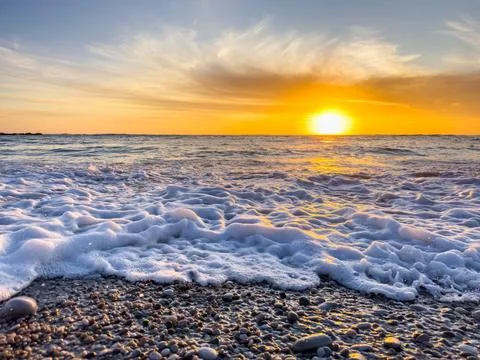Dramatic Golden sunset over tranquil beach, waves lashing the pebble coastlin Stock Photos