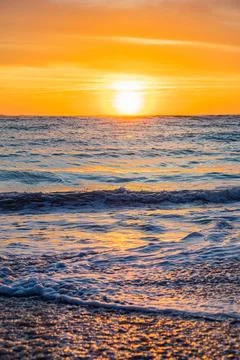 Dramatic Golden sunset over tranquil beach, waves lashing the pebble coastlin Stock Photos