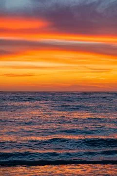 Dramatic Golden sunset over tranquil beach, waves lashing the pebble coastlin Stock Photos