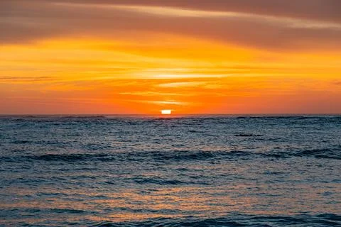 Dramatic Golden sunset over tranquil beach, waves lashing the pebble coastlin Stock Photos