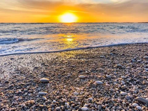 Dramatic Golden sunset over tranquil beach, waves lashing the pebble coastlin Stock Photos