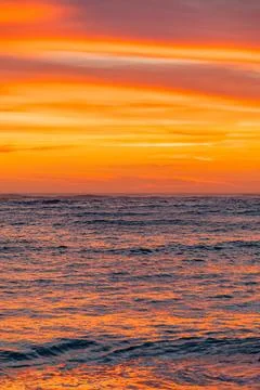 Dramatic Golden sunset over tranquil beach, waves lashing the pebble coastlin Stock Photos