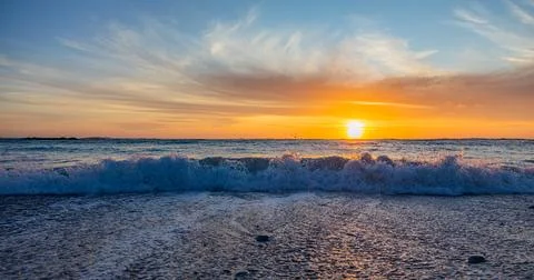 Dramatic Golden sunset over tranquil beach, waves lashing the pebble coastlin Stock Photos