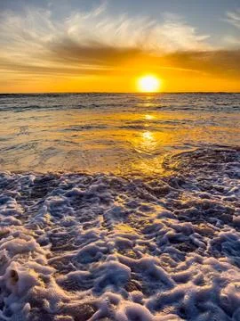 Dramatic Golden sunset over tranquil beach, waves lashing the pebble coastlin Stock Photos