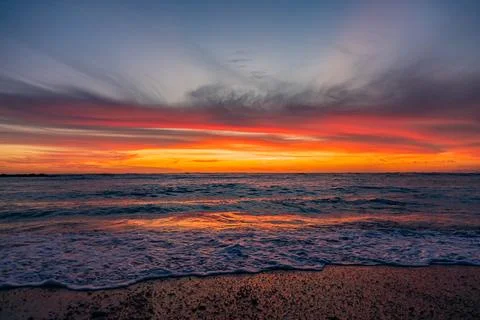 Dramatic Golden sunset over tranquil beach, waves lashing the pebble coastlin Stock Photos