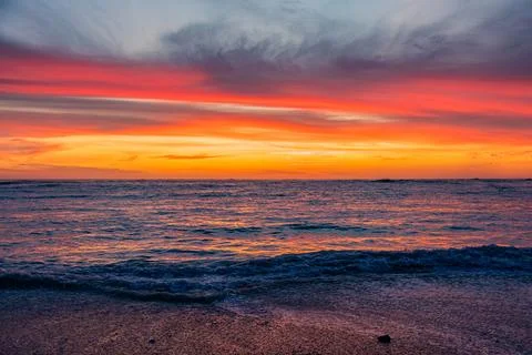 Dramatic Golden sunset over tranquil beach, waves lashing the pebble coastlin Stock Photos