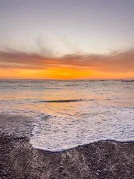 Dramatic Golden sunset over tranquil beach, waves lashing the pebble coastlin Stock Photos