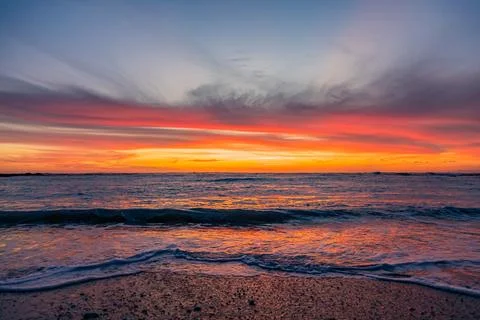 Dramatic Golden sunset over tranquil beach, waves lashing the pebble coastlin Stock Photos